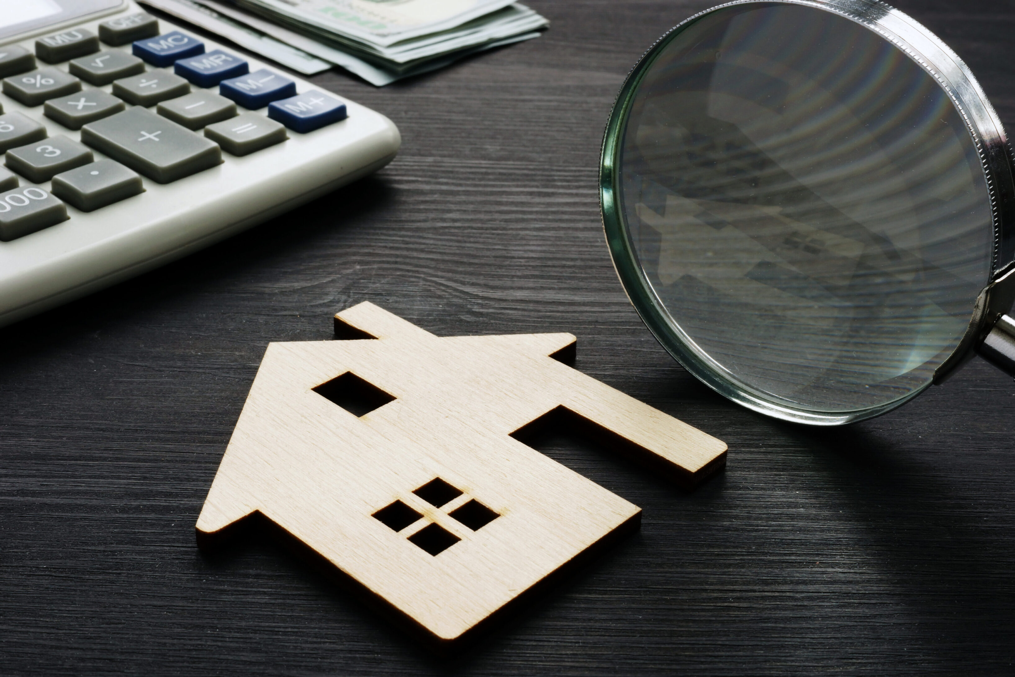 Property assessment. Wooden house with magnifier and calculator. A wooden house sitting on top of a table.